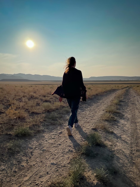 Vista trasera de una mujer caminando por tierra durante la puesta de sol