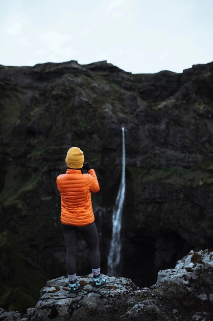 Vista trasera de una mujer capturando una vista de una cascada