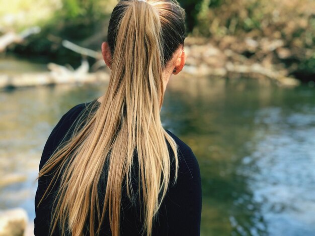 Foto vista trasera de una mujer con cola de caballo mirando al lago