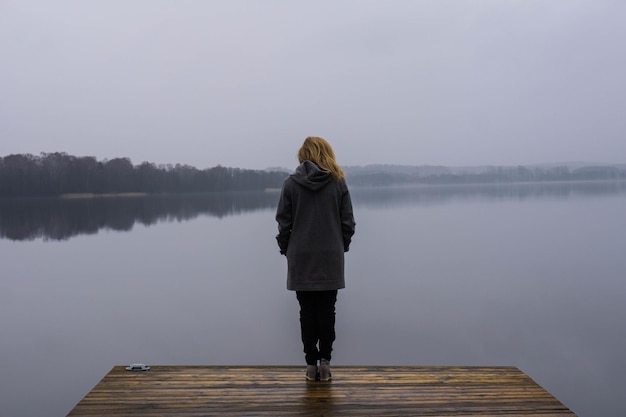 Vista trasera de una mujer en una cubierta de madera contra el lago