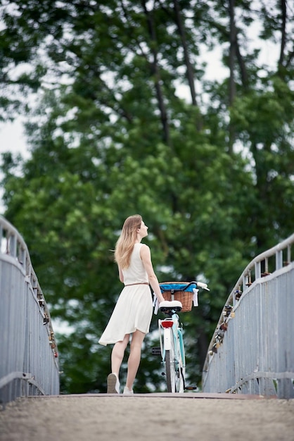 Vista trasera mujer delgada de pie con bicicleta y disfrutando de la naturaleza en el puente