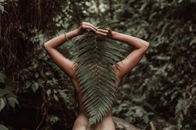 Foto vista trasera de una mujer desnuda sosteniendo hojas en el bosque