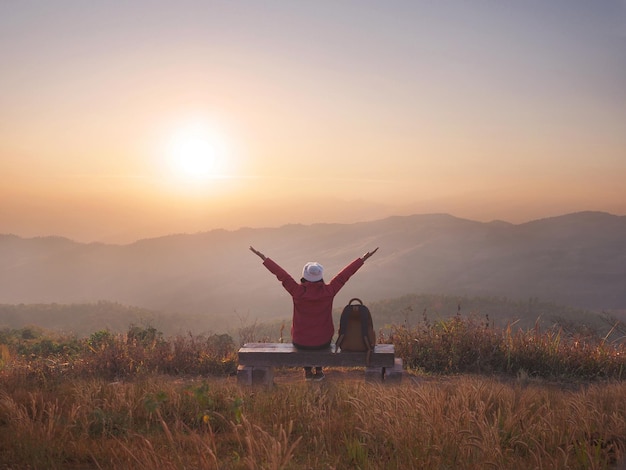 Vista trasera mujer feliz mochilero levantar los brazos al amanecer en la cima de la montaña