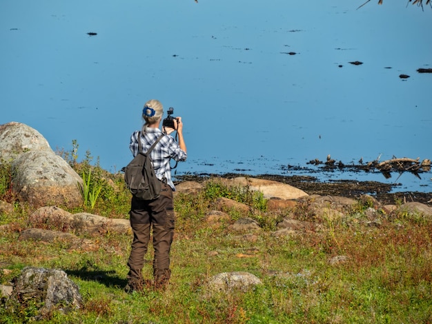 Vista trasera de una mujer fotografiando con una cámara mientras está sentada en el campo