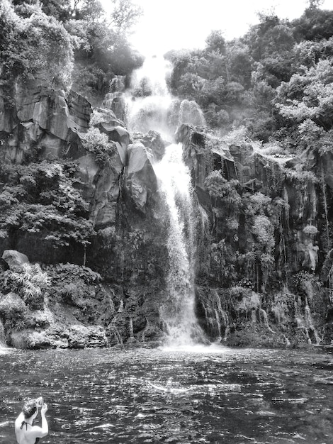 Vista trasera de una mujer fotografiando una cascada