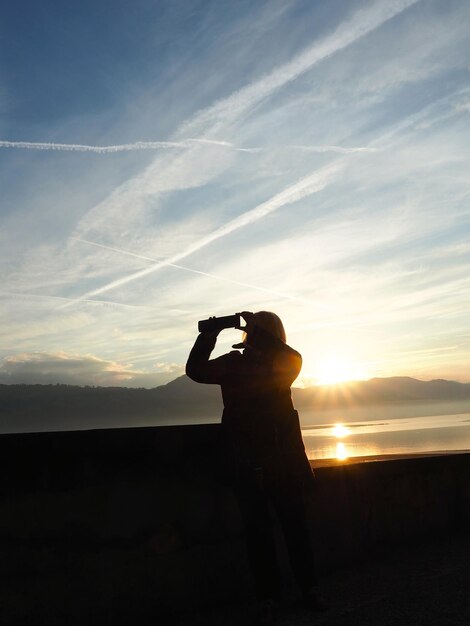 Foto vista trasera de una mujer fotografiando contra un cielo nublado durante la puesta de sol