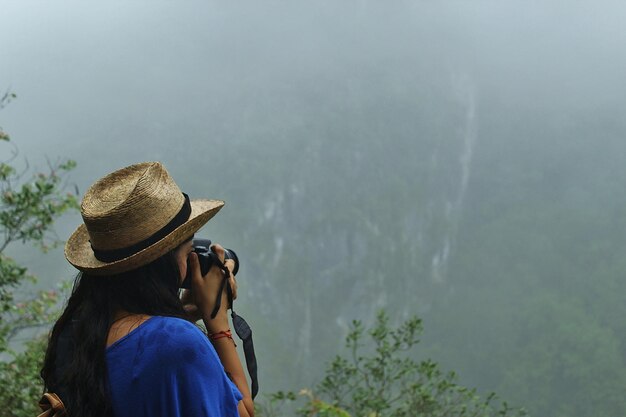 Vista trasera de una mujer fotografiando montañas en tiempo de niebla