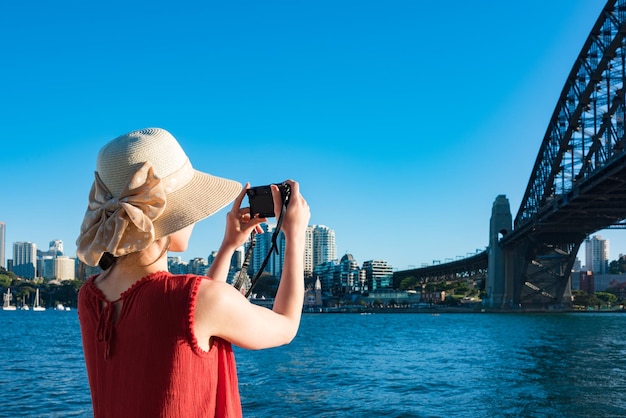 Foto vista trasera de una mujer fotografiando el puente del puerto de sydney contra un cielo despejado