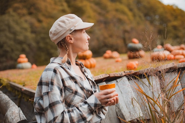 Foto vista trasera de la mujer de un granjero con una taza de bebida mirando calabazas en un campo de calabaza contra el fondo de las montañas