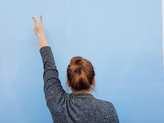 Foto vista trasera de una mujer haciendo un signo de paz contra la pared
