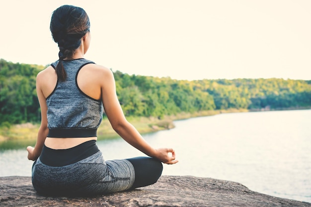 Vista trasera de una mujer haciendo yoga junto al lago