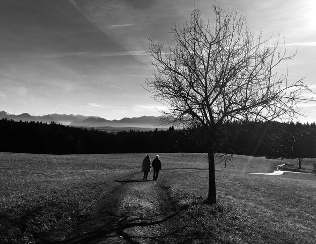 Foto vista trasera de una mujer y un hombre caminando por el campo contra el cielo durante la puesta de sol