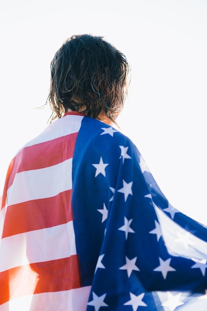 Vista trasera de una mujer irreconocible con el pelo mojado con bandera americana en el muelle contra el mar