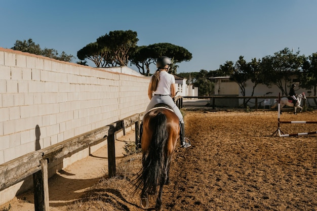 Vista trasera de una mujer jinete calentando con su caballo alrededor de la arena ecuestre