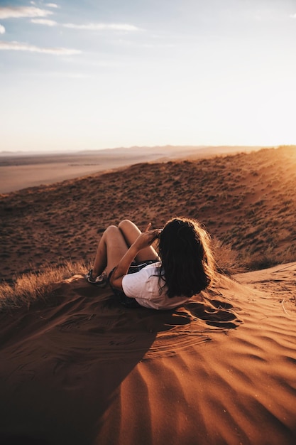 Foto vista trasera de una mujer joven acostada en la arena en el desierto contra el cielo