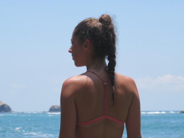 Foto vista trasera de una mujer joven en bikini mirando al mar contra el cielo