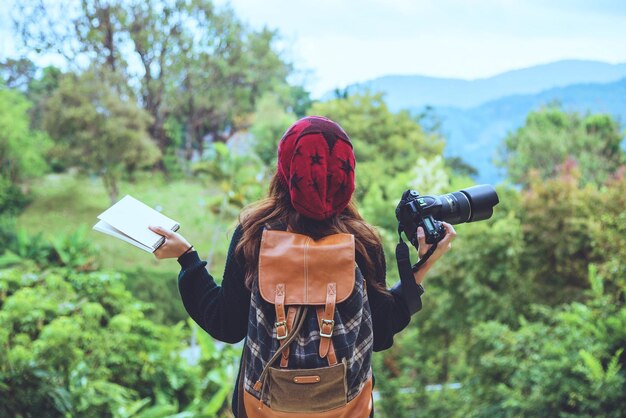 Foto vista trasera de una mujer joven con una cámara de pie contra la montaña