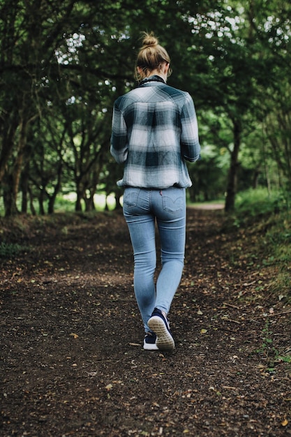 Foto vista trasera de una mujer joven caminando por un camino de tierra en el bosque