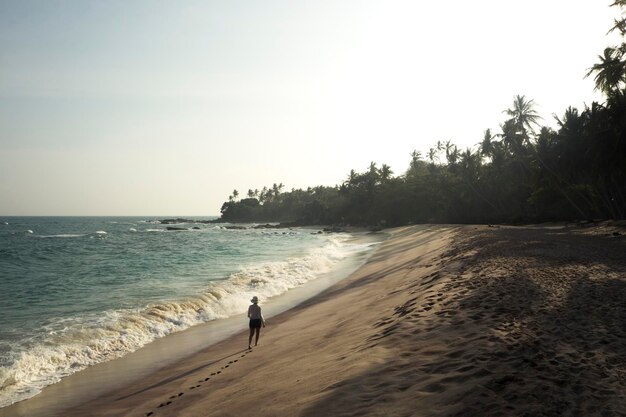 Foto vista trasera de una mujer joven caminando por la orilla en la playa