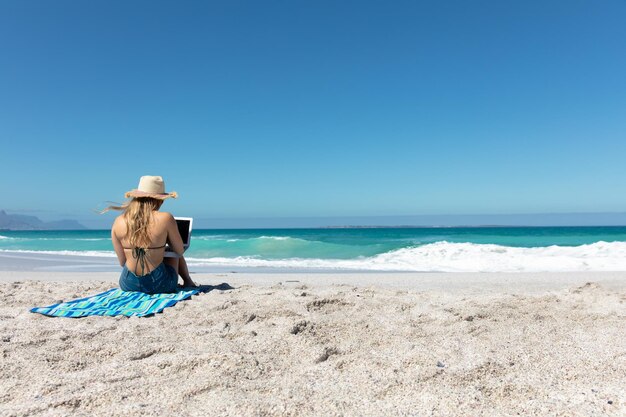 vista trasera, mujer joven, con, computadora, en la playa