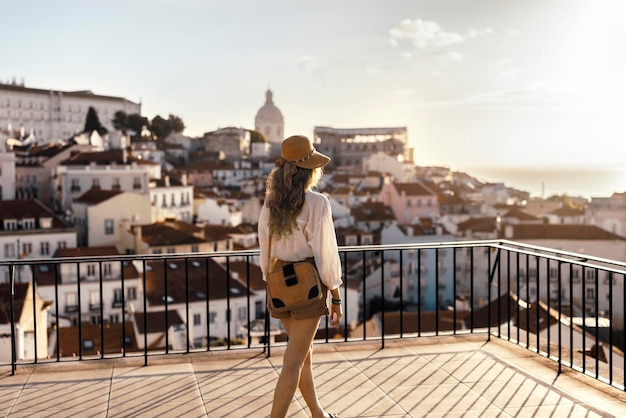 Vista trasera de una mujer joven mirando los edificios de la ciudad contra el cielo durante la puesta de sol