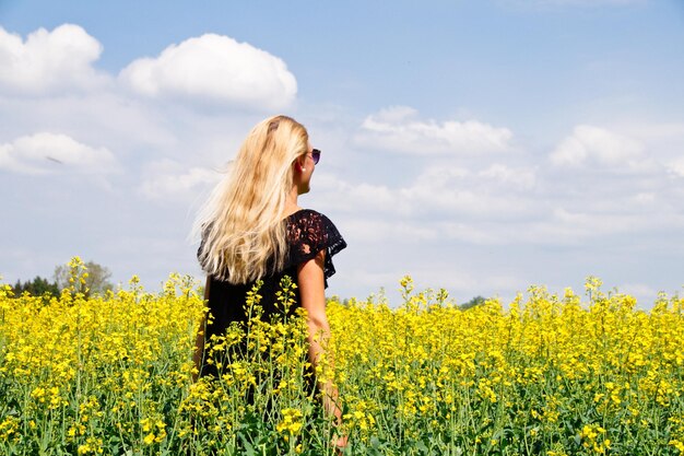 Foto vista trasera de una mujer joven de pie en un campo de colza de semillas oleaginosas