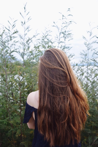 Vista trasera de una mujer joven de pie junto a las plantas contra el cielo