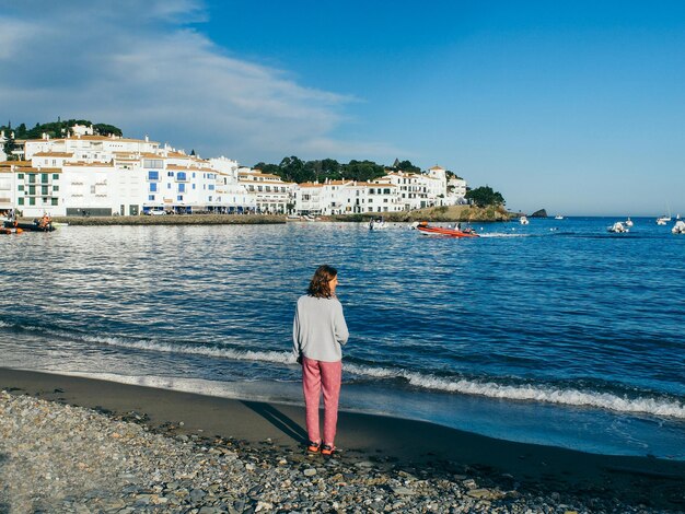 Vista trasera de una mujer joven de pie en la playa contra el cielo