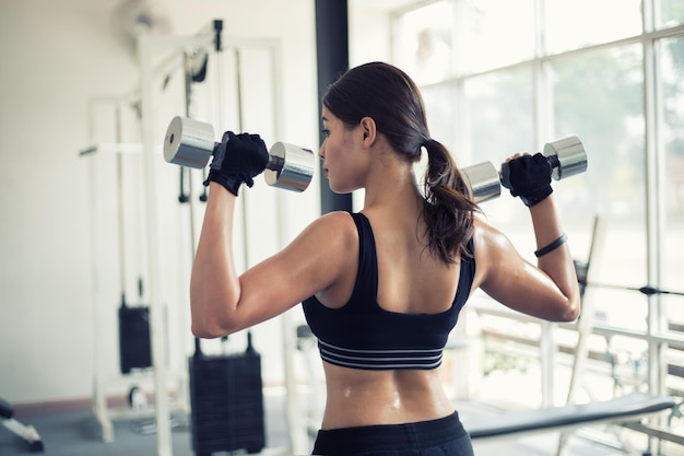 Vista trasera de una mujer levantando pesas en el gimnasio