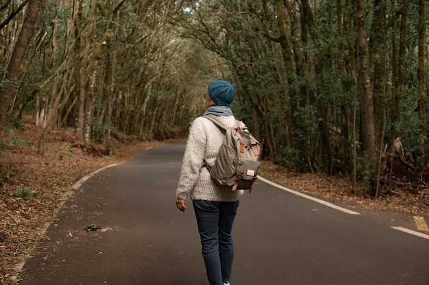 Vista trasera de una mujer madura disfrutando de la libertad al aire libre caminando por una carretera de montaña Anciana activa viajando en un bosque con mochila disfrutando de la naturaleza y las vacaciones