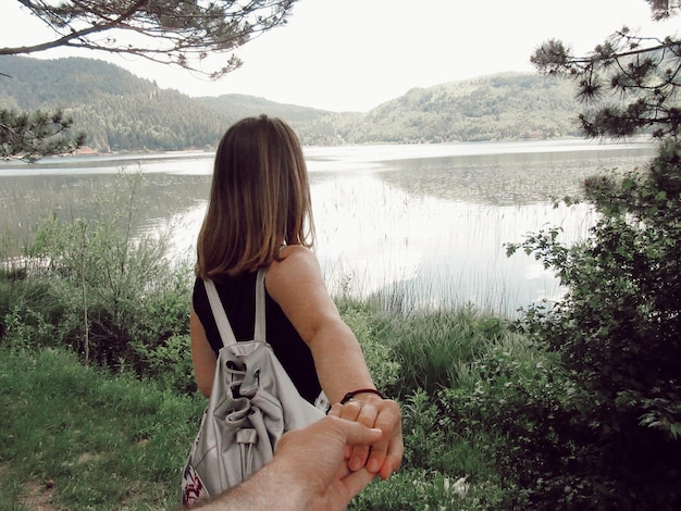 Foto vista trasera de una mujer con la mano en la orilla de un lago en el bosque