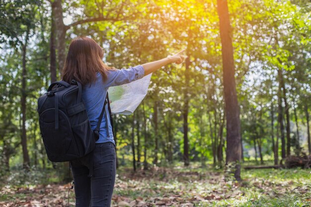 Foto vista trasera de una mujer con un mapa que apunta hacia los árboles en el bosque