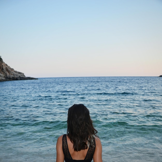 Foto vista trasera de una mujer por el mar contra un cielo despejado