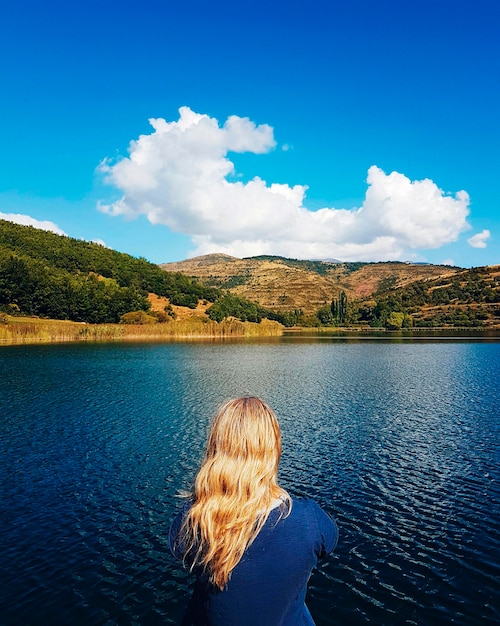 Foto vista trasera de una mujer mirando el lago contra el cielo azul