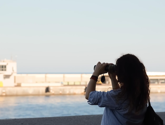 Foto vista trasera de una mujer mirando el mar a través de binoculares contra el cielo