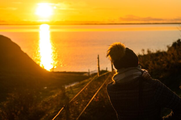 Foto vista trasera de una mujer mirando la puesta de sol sobre el mar