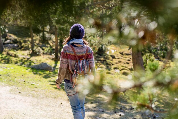 Foto vista trasera de una mujer con mochila caminando por la carretera en el bosque