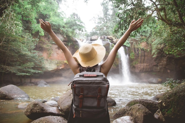 Foto vista trasera de una mujer con mochila mirando una cascada en el bosque