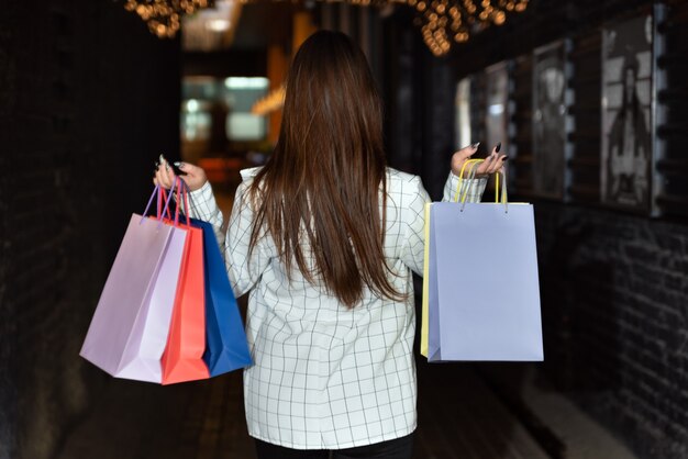 Vista trasera de una mujer morena con bolsas de papel de colores en sus manos.