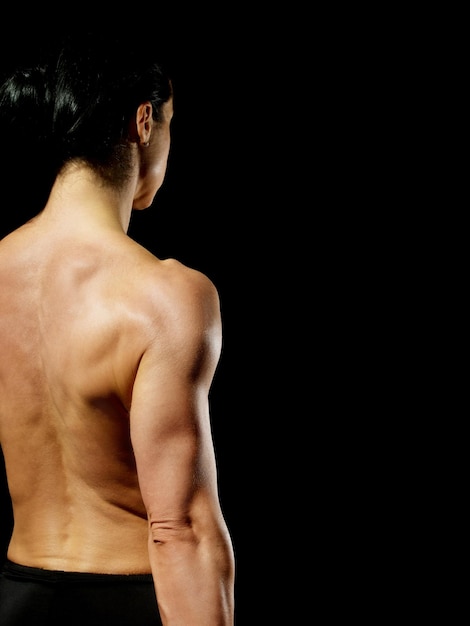 Foto vista trasera de una mujer musculosa en topless de pie contra un fondo negro