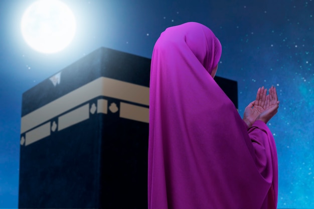 Foto vista trasera de la mujer musulmana asiática en un velo de pie y rezando con vista de kaaba y fondo de escena nocturna