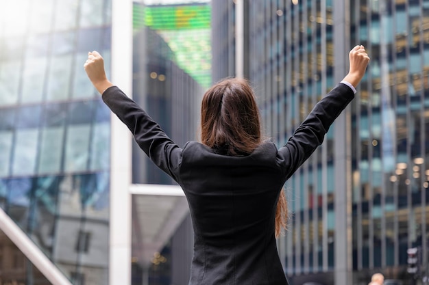 Foto vista trasera de una mujer de negocios con los brazos levantados de pie contra edificios modernos