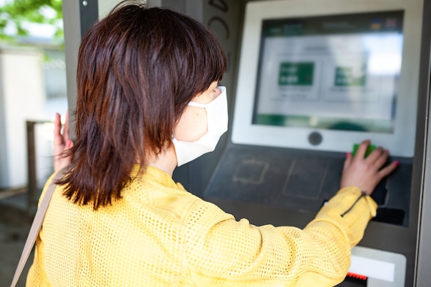 Vista trasera de una mujer no identificada con una máscara protectora apunta con el dedo al tablero de información borrosa con instrucciones para la protección contra el coronovirus