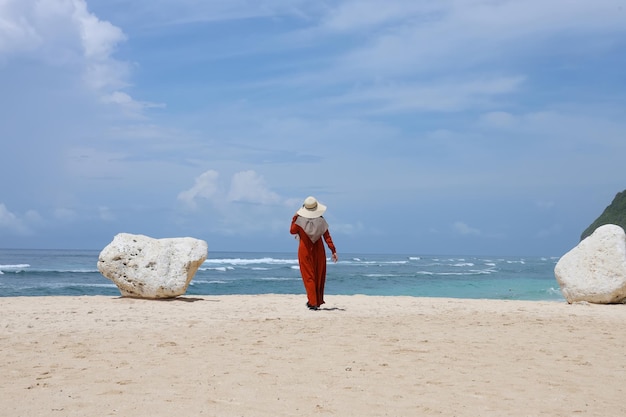 Vista trasera de una mujer parada a lo largo de una playa de arena mientras usa un sombrero de paja.