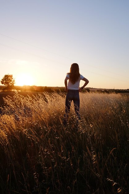 Vista trasera de una mujer de pie en el campo contra el cielo durante la puesta de sol