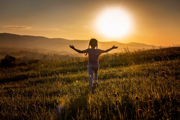 Vista trasera de una mujer de pie en el campo contra el cielo durante la puesta de sol