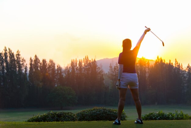 Foto vista trasera de una mujer de pie en un campo de golf contra el cielo durante la puesta de sol.