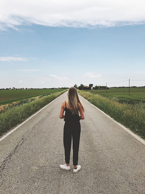 Vista trasera de una mujer de pie en la carretera contra el cielo