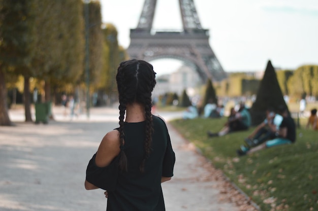 Foto vista trasera de una mujer de pie en la carretera contra la torre eiffel en la ciudad