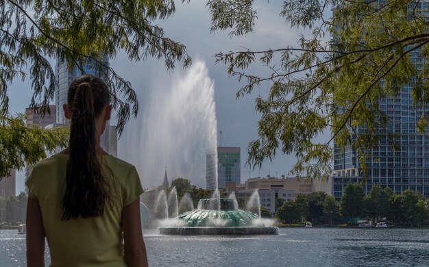 Vista trasera de una mujer de pie contra una fuente en el parque del lago eola